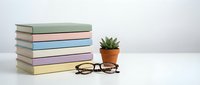 Stack of colorful books with reading glasses and small potted succulent plant on white desk surface for education and learning concepts.