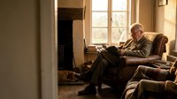 Senior Caucasian man reading book in comfortable leather armchair by window in cozy living room with warm natural lighting for relaxation and leisure concepts.