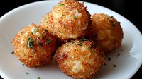 Crispy golden potato croquettes garnished with fresh herbs and seasonings on white plate, close up view showing crunchy breaded exterior and soft interior.