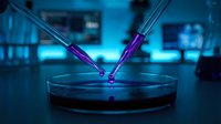 Two pipettes dispensing purple liquid into a petri dish in a laboratory setting with blue-toned scientific equipment and glowing displays in the background, suitable for biotech, research, and medical applications.