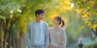 Young Asian couple walking together in autumn park, sharing romantic moment amid golden sunlight and fall foliage, expressing genuine joy and connection.