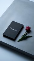 Elegant black thank you card beside a red tulip on a concrete surface, conveying gratitude and minimalist style for events and branding.