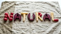Word NATURAL spelled with fresh vegetables including radishes, beets and parsnips on rustic linen fabric, organic food concept.