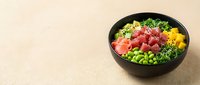 Colorful poke bowl with raw tuna, edamame, avocado, cucumber, and sesame seeds on beige surface. Fresh Hawaiian cuisine for restaurants, food blogs, and healthy eating content.