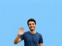Young man with dark curly hair and olive complexion wearing navy t-shirt, waving hand in friendly greeting against bright blue background. Suitable for greeting, welcome, and friendly communication concepts.