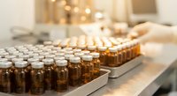 Rows of amber glass vials in pharmaceutical manufacturing facility with sterile production line and quality control equipment in background.