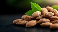 Fresh raw almonds with green leaves on dark background, dramatic lighting creates appetizing mood for healthy eating and natural food photography.