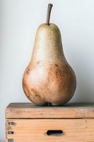 Fresh ripe pear with speckled skin and brown stem displayed on rustic wooden box against neutral background.