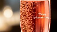 Champagne glass with bubbles and Happy Anniversary text for romantic celebration milestone greeting card design with elegant golden bokeh background.