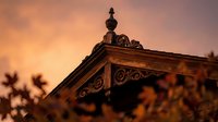 Ornate wooden roof detail with decorative carved elements against warm sunset sky creating atmospheric architectural photography for heritage design projects.