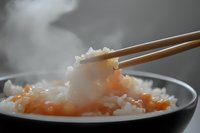 Steaming hot rice with salmon pieces being picked up by wooden chopsticks from a black bowl, creating a delicious Asian cuisine moment.