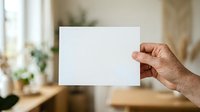 Caucasian male hand holding blank white card in modern home interior with natural light and blurred background for mockup or branding purposes.