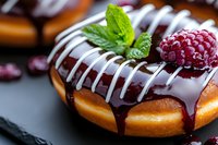Fresh raspberry and mint leaf garnish on chocolate glazed donut with white drizzle, extreme close up on dark background showing texture and shine.