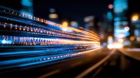 Dynamic light trails streak across urban nightscape with glowing blue and orange streaks creating futuristic motion effect against blurred city background.