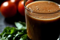 Fresh tomato juice in glass with ripe red tomatoes and green herbs on dark background. Healthy organic vegetable drink for breakfast and diet nutrition.