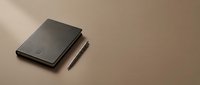 Closed black leather notebook with pen on neutral beige background, minimalist flat lay composition for business, stationery, and office design projects.