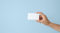 Hand holding blank white business card against light blue background for branding and corporate identity mockup purposes.