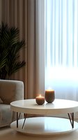 Cozy minimalist living room corner with round white coffee table, lit candles, and palm plant. Soft natural light through sheer curtains creates peaceful atmosphere.