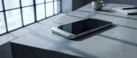 Modern smartphone lying on concrete surface in minimalist office workspace with natural window light creating shadows and contemporary atmosphere.