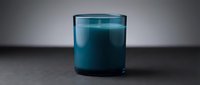 Teal scented candle in glass jar on dark surface with gradient background for home decor and aromatherapy relaxation.