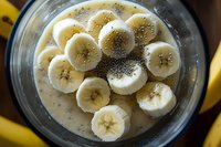 Fresh banana slices and chia seeds floating in creamy smoothie bowl captured from above, healthy breakfast preparation with nutritious ingredients.