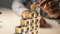Professional businessman building tower with transparent cubes containing golden dollar symbols representing financial growth and investment strategy.