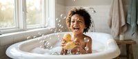 Happy African American toddler boy playing with rubber duck toy in bathtub with soap bubbles, enjoying bath time in bright bathroom with natural window light.