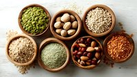 Assortment of nutritious seeds, nuts, and legumes in wooden bowls on white background, showcasing healthy plant-based protein sources for cooking.
