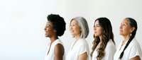 Diverse group of women in white clothing standing together in profile view, representing unity, empowerment and sisterhood across different ages and ethnicities.