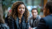 Young African American businesswoman with curly hair and bright smile at corporate meeting, wearing plaid blazer. Professional networking and workplace diversity concept for business marketing.