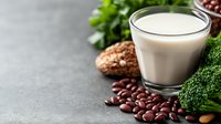 Glass of fresh milk with scattered coffee beans, chocolate cookies and green broccoli on dark concrete background, selective focus with copy space.