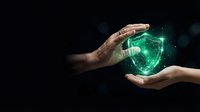 Hand holding glowing green shield with digital particles on dark background, representing cybersecurity, data protection, and network safety for technology concepts.