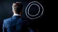 Businessman in dark suit looking at glowing circular shape drawn on black background, representing goals, targets and business vision concept.