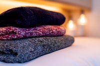 Stack of folded warm knitted winter socks in purple, burgundy and gray colors on white surface with soft bokeh lights in background, cozy seasonal concept.