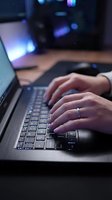 Hands typing on laptop keyboard in modern office workspace with blurred monitor screens in background for business and technology concepts.