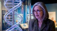Middle-aged Caucasian female scientist with glasses examining DNA double helix hologram in modern laboratory for genetic research and biotechnology studies.