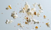 Flying popcorn kernels scattered on light background with butter and salt particles creating dynamic composition for food advertising and menu design.