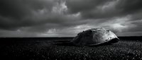 Dramatic black and white seascape with large boulder on pebble beach under stormy cloudy sky. Moody coastal landscape for artistic projects.