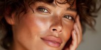 Young woman with freckles and curly hair touching face in natural light. Beauty skincare portrait with glowing skin and gentle expression for wellness content.