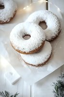 Powdered sugar donuts on white parchment paper with holiday decorative elements and pine branches, creating festive winter mood for seasonal baking and treats.
