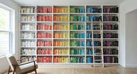 Modern home library with rainbow organized bookshelf displaying colorful book collection in bright reading room with wooden chair and natural window light.