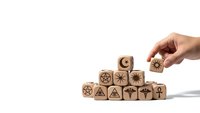 Hand placing wooden cube with gear symbol completing pyramid of blocks featuring business and strategy icons on white background.
