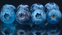 Fresh ripe blueberries with water drops and reflection on dark background, macro photography showing detailed texture and natural patterns in cool blue tones.