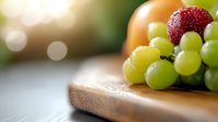 Fresh ripe strawberry and green grapes on wooden cutting board against blurred background with soft bokeh lights, macro food photography.