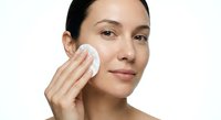 Young Hispanic woman applying skincare product with cotton pad on white background for beauty and wellness routine.