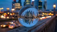 Transparent crystal sphere reflecting illuminated downtown skyline with skyscrapers at dusk, bokeh city lights in background, urban nighttime scene for architectural and business concepts.