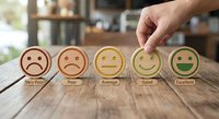 Customer feedback rating system with hand selecting excellent smiley face from very poor to excellent scale on wooden table for service quality evaluation.