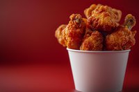 Crispy fried chicken wings in white paper bucket against dark red background. Golden brown, crunchy coating with selective focus and copy space for menu design.