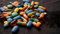 Colorful pharmaceutical pills and capsules scattered on dark fabric surface for medical healthcare and medication concepts.