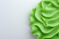 Swirled light green frosting or cream texture with delicate sparkles on white background, macro shot showing soft waves and curves. Isolated food decoration element.